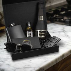 a black box with sunglasses, flasks and other items sitting on a marble counter top