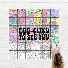 a girl is holding up an egg - filled to see you poster in front of a white brick wall