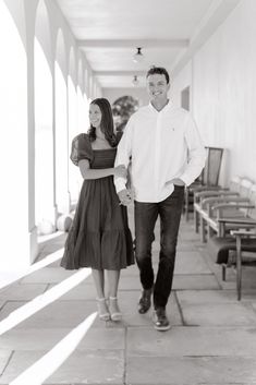 a man and woman walking down a long hallway holding hands, black and white photo