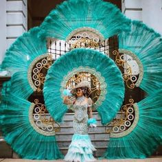 a woman in a blue and gold dress standing next to a peacock fan with feathers on it