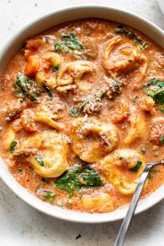 a white bowl filled with pasta and spinach in tomato sauce on top of a table