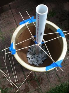 a cup with sticks sticking out of it sitting on the ground next to some rocks