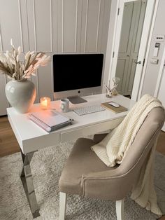 a white desk with a computer on it and a vase filled with flowers next to it