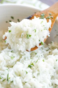 a wooden spoon full of white rice with herbs in it and on top of the bowl