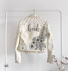 a white jacket hanging on a rack with flowers and the word bride written on it