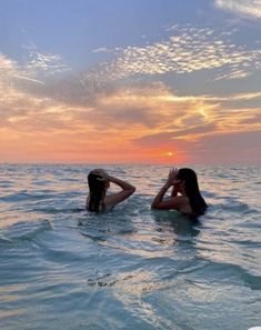 two people are in the water at sunset