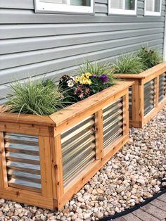 two wooden planters filled with plants next to a gray house and gravel area on the ground