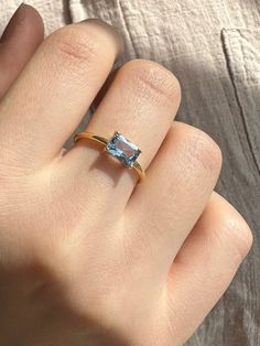 a woman's hand wearing a gold ring with an aqua blue topazte