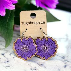 "Adorn your ears with the elegance of our 'Regal Petals' earrings, featuring the exotic beauty of the purple hibiscus. These scalloped wooden earrings are a canvas for the mesmerizing shades of purple that paint each detailed petal, centered with a delicate white highlight to bring the bloom to life. The intricate edges mirror the hibiscus flower's natural grace, creating a pair of earrings that are as captivating as they are unique. Ideal for those who appreciate the splendor of nature's artistry, these earrings are a stylish tribute to the tropics. Beautiful handmade, hand-painted dangle earrings. These are 1/8\" maple wood 2 3/4\" drop, findings made of stainless steel so no need to worry about tarnishing or allergic reaction. Indulge in the artisanal allure of our handmade wood engrave Purple Flower-shaped Pierced Earrings, Purple Flower Shaped Earrings, Purple Hypoallergenic Flower Drop Earrings, Purple Hypoallergenic Drop Flower Earrings, Hypoallergenic Purple Flower Drop Earrings, Purple Hibiscus, Ashley Nicole, Hand Painted Earrings, Allergic Reaction