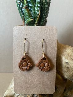 a pair of brown earrings sitting on top of a wooden stand next to a plant