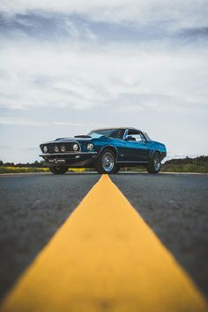 an old blue car is parked on the side of the road in front of a yellow line