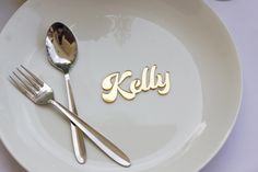 a white plate topped with two silverware and a name spelled in gold on it