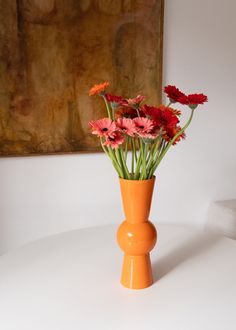 an orange vase filled with flowers on top of a white table