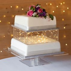 two tiered white cake with pink and purple flowers on top, surrounded by fairy lights