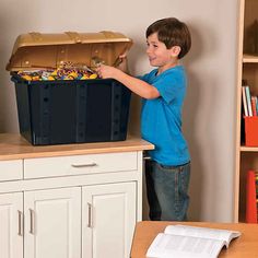 a young boy is holding a bin full of legos and looking at the contents in it