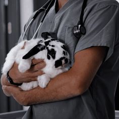 a veterina holding a black and white rabbit in his arms while wearing a stethoscope