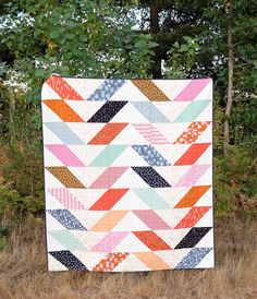 a colorful quilt sitting on top of a field next to some tall grass and trees