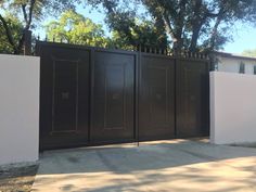 a white fence with black gates in front of trees and bushes on the other side