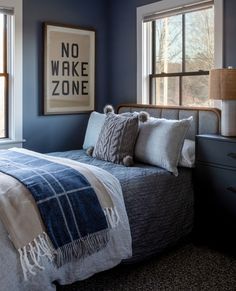 a bedroom with blue walls and white bedding, two windows, and a no wake zone poster on the wall