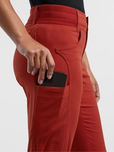 a woman in red pants is holding her cell phone and looking at the side pocket