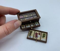 a hand is holding an open box with miniature items in it on a white surface