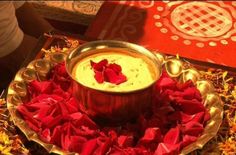 a bowl filled with dip surrounded by red petals on top of a gold platter