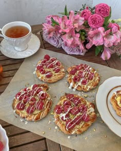 four waffles are sitting on a table next to some pink flowers and a cup of tea