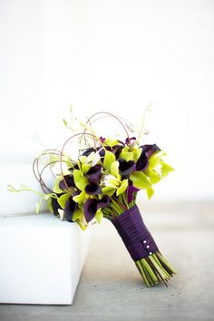 a bouquet of purple and yellow flowers sitting on top of a white bench next to a wall