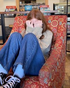 a woman sitting in a red chair with her hands on her face while looking at the camera