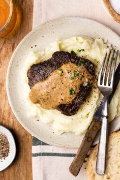 a white plate topped with mashed potatoes covered in gravy next to a fork