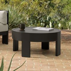 a black coffee table sitting on top of a brick floor next to a chair and potted plant