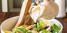 a person pouring dressing into a salad in a bowl with lemon wedges on the side