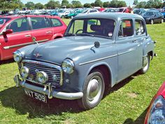 an old blue car parked in a field next to other red and white cars at a car show