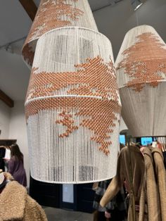 two white and orange lamps hanging from the ceiling in a room with people looking at them