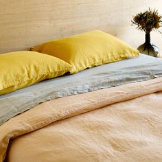 a bed with two yellow pillows on top of it next to a vase filled with flowers