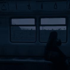 a woman sitting on a train looking out the window at night, with her back turned to the camera