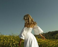 a woman in a white dress walking through a field full of yellow wildflowers