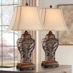 two lamps sitting on top of a wooden table next to a window with curtains in the background