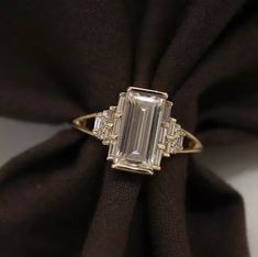 an emerald and diamond ring sitting on top of a black cloth with gold trimming