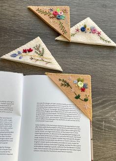 an open book sitting on top of a wooden table next to three pieces of embroidered fabric