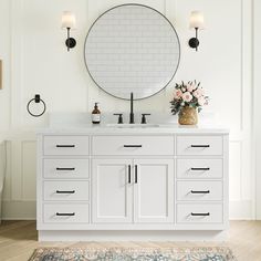 a white bathroom vanity with a round mirror above it and flowers on the counter top