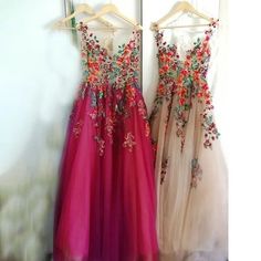 two dresses hanging up on a rack in front of a door, one is pink and the other is red