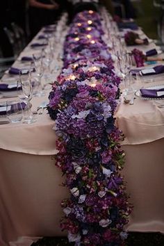 a long table covered in purple flowers and wine glasses is set up for a formal dinner