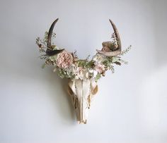 an animal skull with flowers and antlers on it's head against a white wall