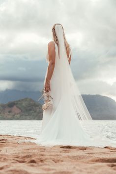 a woman in a wedding dress standing on the beach