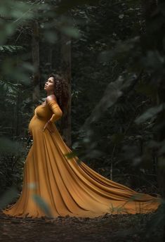 a pregnant woman in a yellow dress standing in the woods