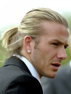 a man in a suit and tie with his hair pulled into a ponytail, looking off to the side