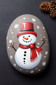 a painted rock with a snowman wearing a red hat and scarf on top of it