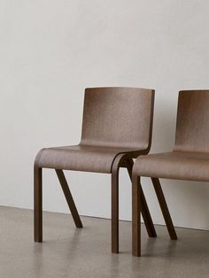 two wooden chairs sitting next to each other on a cement floor in front of a white wall