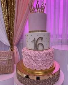 a pink and gold birthday cake with a tiara on top is sitting on a table